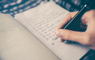 Eine Hand trägt Aufgaben in eine To-Do-Liste ein, um den bevorstehenden Familienurlaub zu planen und zu organisieren.