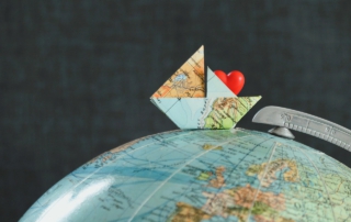 Origami-Boot aus einer Weltkarte mit einem roten Herz auf einem Globus, symbolisiert Reisen und Liebe.